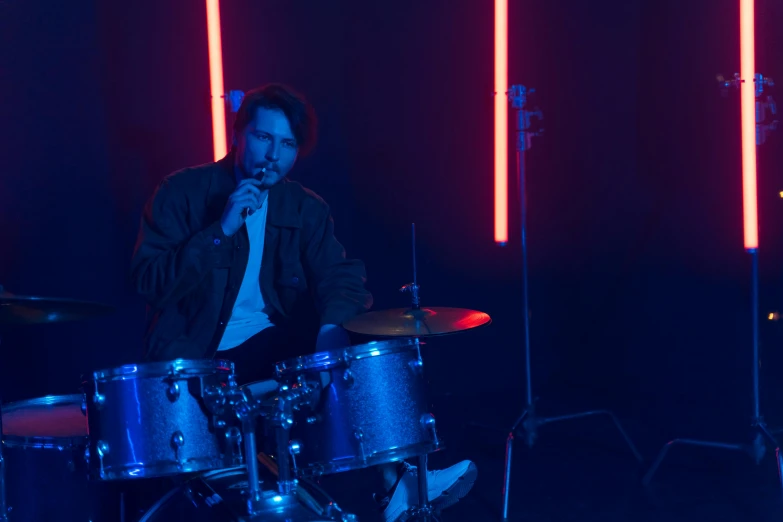 a man sitting on top of a drum set, cinematic blue lighting, mark edward fischbach, neon background lighting, b - roll