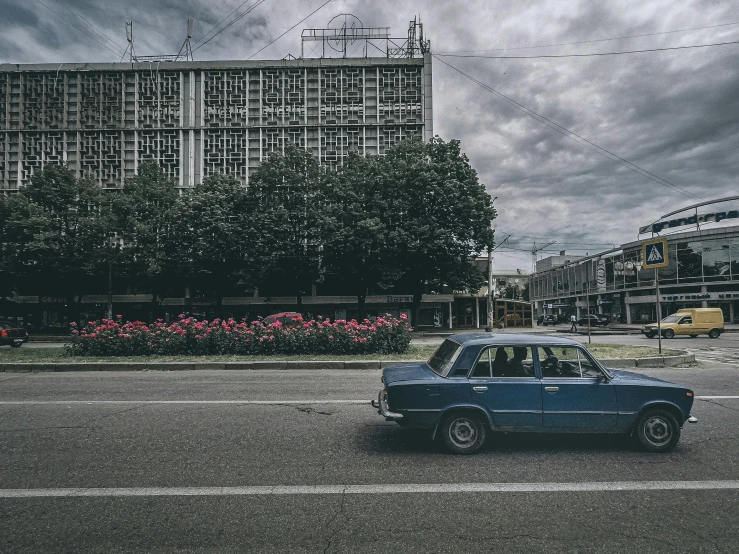 a blue car driving down a street next to a tall building, an album cover, by Sven Erixson, unsplash contest winner, brutalism, russian lada car, 000 — википедия, square, historical