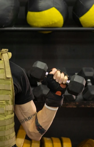 a man holding two dumbbells in a gym, by Dan Luvisi, reddit, combat vest, high quality photo, b - roll, profile image