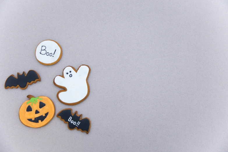 a group of decorated cookies sitting on top of a table, a cartoon, by Emma Andijewska, pexels, halloween decorations, background image, on a gray background, minimalistic art