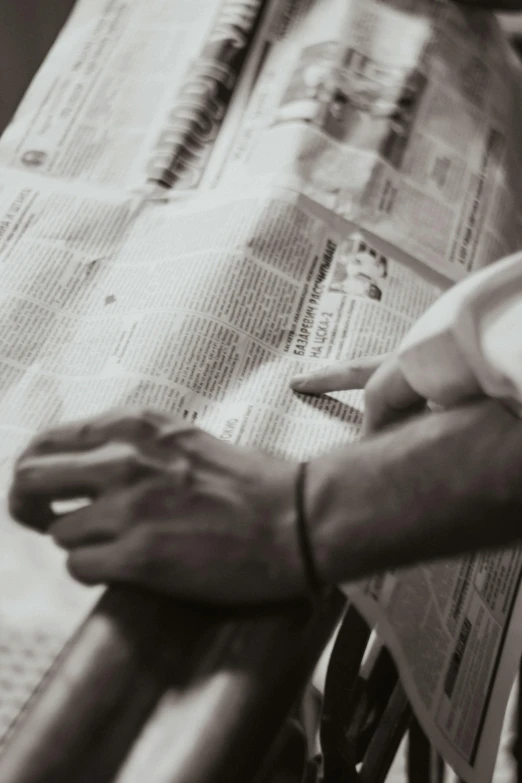 a man sitting on a bench reading a newspaper, a black and white photo, unsplash, hands on counter, pointing, craftsmanship, blurred