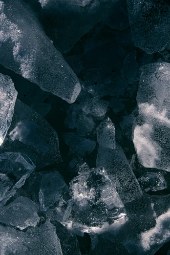 a pile of ice sitting on top of a pile of rocks, trending on unsplash, crystal cubism, dark blue tones, black, grey, female made of ice