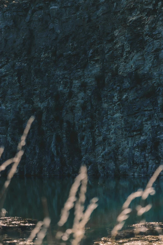 a man sitting on top of a rock next to a body of water, inspired by Elsa Bleda, unsplash contest winner, texture detail, dark cavern, small reeds behind lake, 8k detail