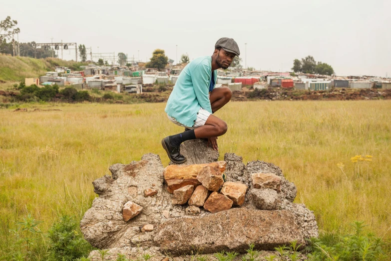 a man squatting on a pile of rocks in a field, inspired by Joze Ciuha, land art, standing in township street, press shot, pondering, urban planning