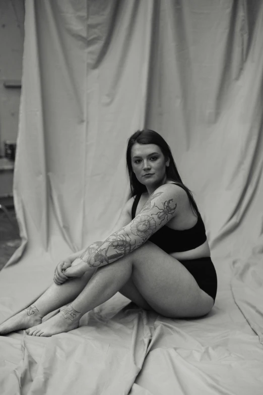 a black and white photo of a woman with tattoos, a black and white photo, by Jessie Alexandra Dick, thick thighs, florence pugh, sitting pose, loin cloth