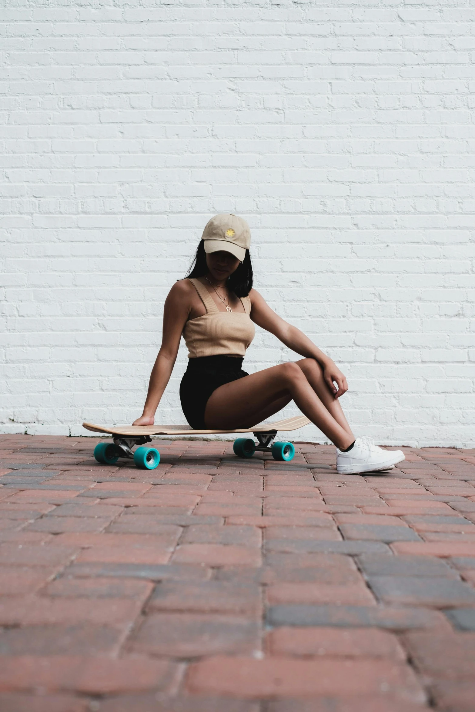 a woman sitting on a skateboard in front of a white brick wall, trending on unsplash, slightly tanned, wearing a crop top, white straw flat brimmed hat, teal