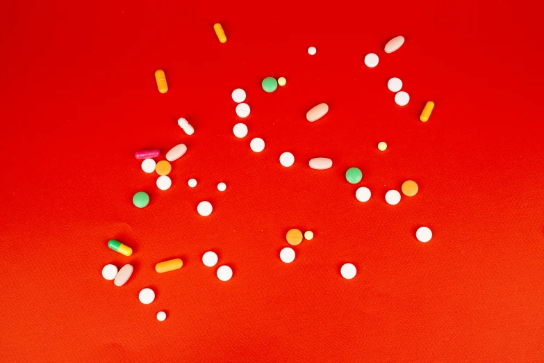 a bunch of pills on a red surface, by Julia Pishtar, antipodeans, multicoloured, red, multicolored