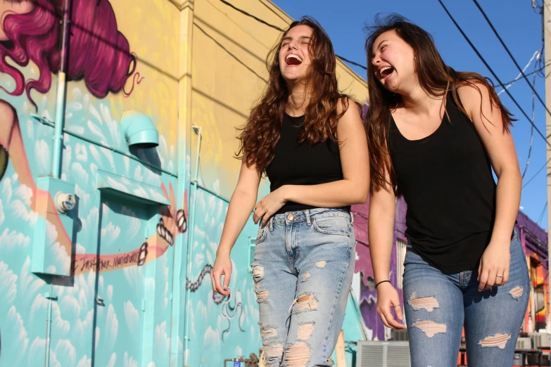 a couple of women standing next to each other on a skateboard, an album cover, by Meredith Dillman, pexels contest winner, graffiti, earing a shirt laughing, colorful mural on walls, teenager hangout spot, profile image
