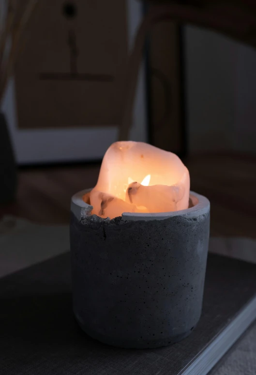 a lit candle sitting on top of a book, inspired by Sarah Lucas, concrete art, glowing crystal on a rock, close-up product photo, grey, made of cement