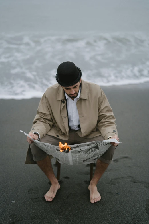 a man sitting on a beach reading a newspaper, an album cover, unsplash, renaissance, playing with fire, magician, sadness, standing beside the ocean