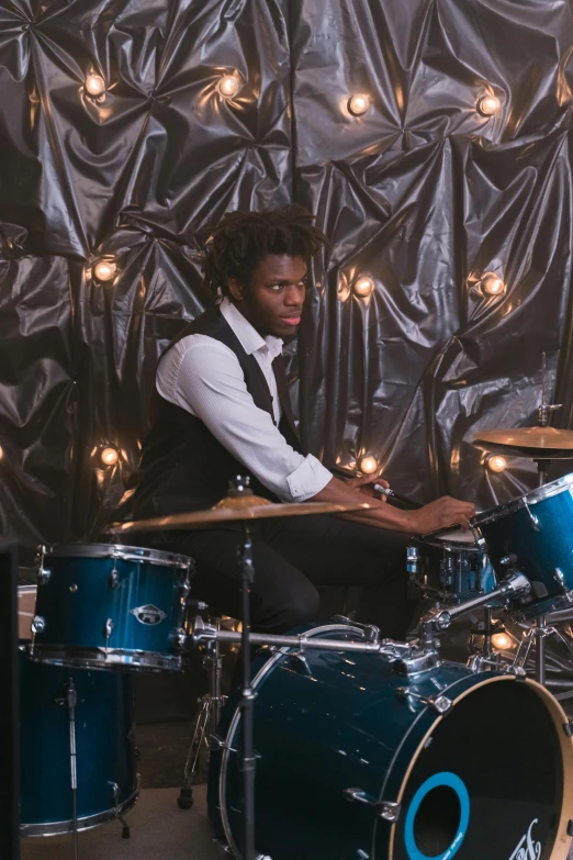 a man sitting in front of a drum kit, american gods, in style of tyler mitchell, hammershøi, set photograph