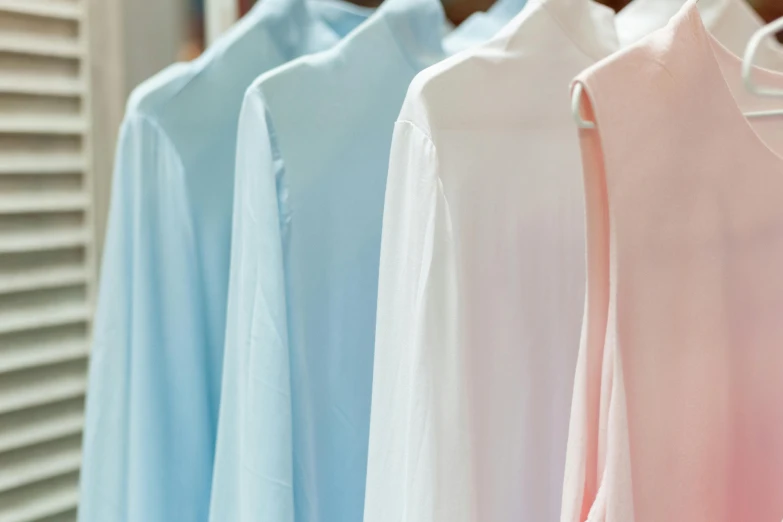 a row of shirts hanging on a clothes rack, by Alice Mason, trending on unsplash, private press, pastel blues and pinks, wearing white robes, plain uniform sky at the back, flowing shimmering fabrics