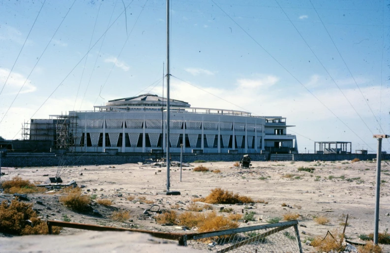 a large building sitting in the middle of a desert, a colorized photo, flickr, brutalism, stadium setting, government archive photograph, shoreline, pavilion