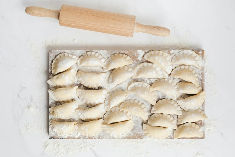 a wooden rolling pin sitting on top of a cutting board, inspired by Károly Patkó, trending on pexels, mingei, dumplings on a plate, in rows, covered in white flour, served with pasta