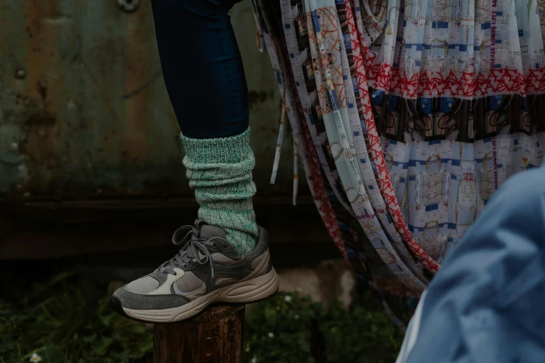 a woman standing on top of a wooden post, by Jessie Algie, trending on unsplash, acid-green sneakers, paisley, blue and grey tones, sitting down casually