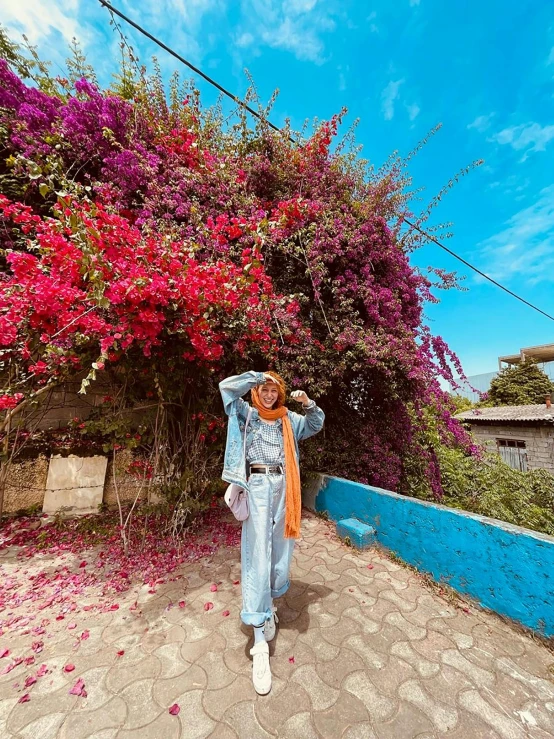 a woman standing in front of a blue wall, an album cover, pexels contest winner, bougainvillea, wearing dirty travelling clothes, 👰 🏇 ❌ 🍃, scenic colorful environment