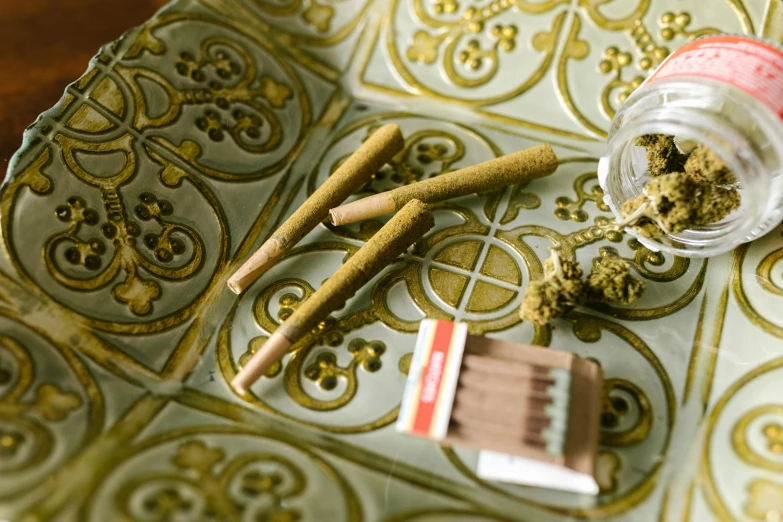 a container of marijuana sitting on top of a table, a still life, inspired by William Harnett, unsplash, renaissance, patterned, cigars, green and gold, high angle close up shot