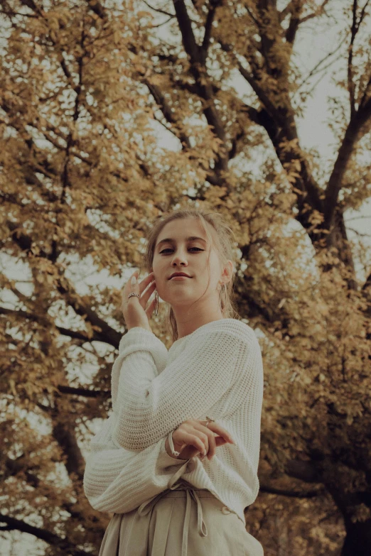 a woman standing in front of a tree talking on a cell phone, by Niko Henrichon, pexels contest winner, realism, portrait of white teenage girl, beige and gold tones, autum, wearing a white sweater