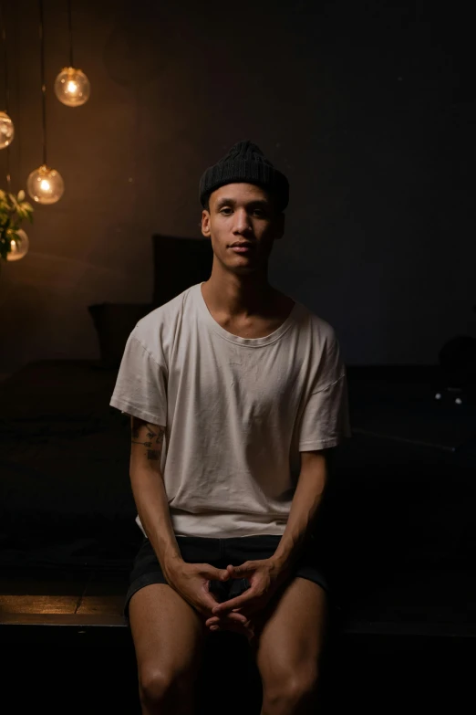 a man sitting on a bench in a dark room, a portrait, unsplash, meditating pose, around 1 9 years old, standing in a dimly lit room, slightly tanned