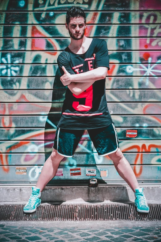 a man standing in front of a graffiti covered wall, by Julia Pishtar, pexels contest winner, wearing shorts and t shirt, kawaii playful pose of a dancer, rated t for teen, wearing basketball jersey