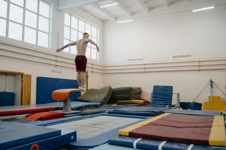 a man standing on a balance beam in a gym, by Matija Jama, arabesque, center of picture, dingy gym, lachlan bailey, open room