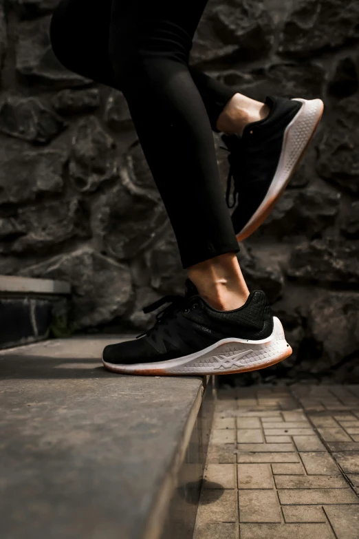 a person standing on a step next to a stone wall, a picture, by Adam Marczyński, unsplash contest winner, new balance pop up store, black and terracotta, sauroform hybrid, dynamic active running pose