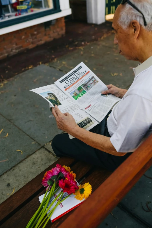 a man sitting on a bench reading a newspaper, a picture, by Dan Content, unsplash, private press, cover photo portrait of du juan, flowers around, high angle shot, in australia