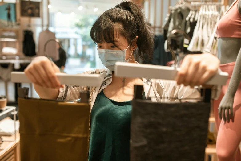 a woman wearing a face mask in a clothing store, by Nicolette Macnamara, pexels contest winner, happening, carrying a tray, gemma chen, sea - green and white clothes, holding a crowbar