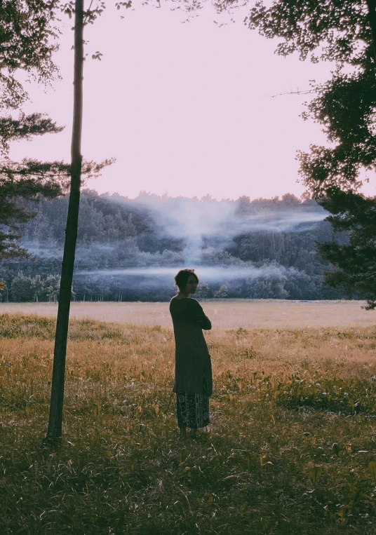 a person standing in a field next to a tree, inspired by Elsa Bleda, pexels contest winner, in front of a forest background, grainy movie still, looking off into the distance, concert