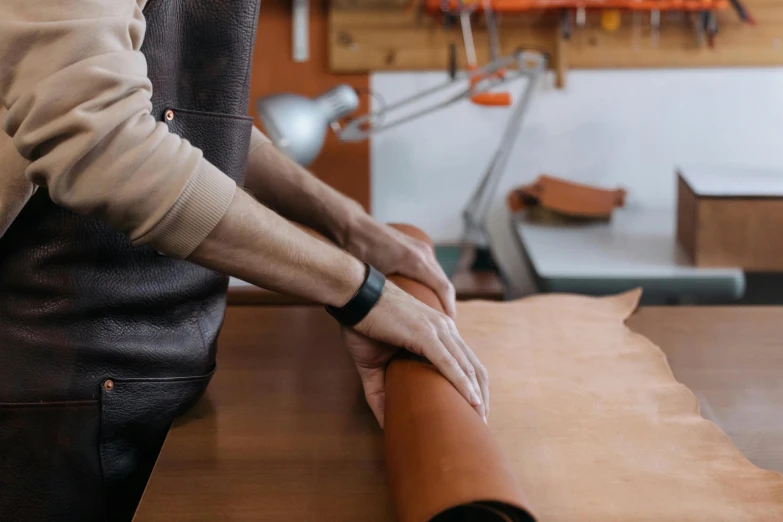 a close up of a person cutting a piece of leather, trending on pexels, arts and crafts movement, hands behind back, sitting on a table, “the ultimate gigachad, thumbnail