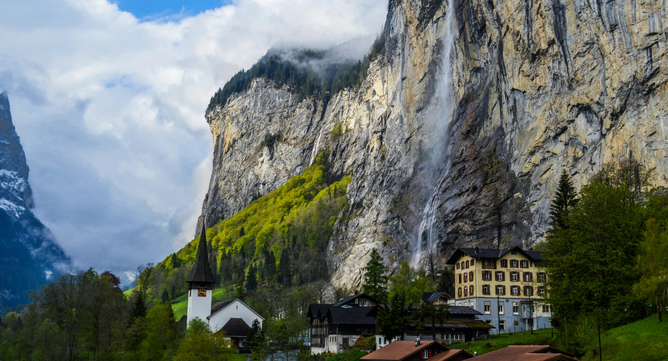 a group of houses sitting on top of a lush green hillside, by Johannes Voss, pexels contest winner, art nouveau, lauterbrunnen valley, waterfall falling into a lake, white marble buildings, slide show