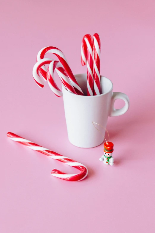 a cup filled with candy canes next to a candy cane, inspired by Cerith Wyn Evans, mini figure, with a straw, pink iconic character, medium level shot