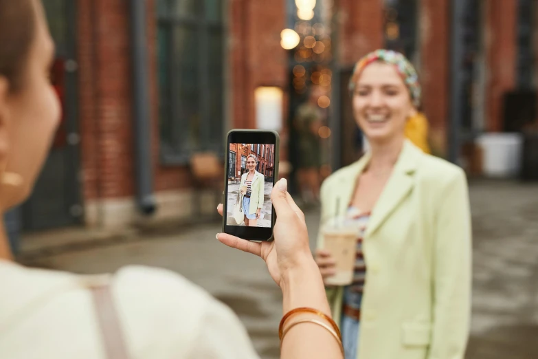 a woman taking a picture of another woman with a cell phone, a picture, trending on pexels, 🤠 using a 🖥, promotional image, outdoor photo, a still of a happy