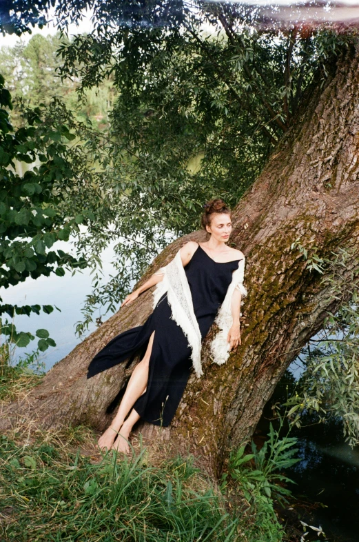 a woman in a black dress leaning against a tree, inspired by Konstantin Somov, unsplash, renaissance, on a lake, at a fashion shoot, wearing a toga and sandals, eleanor tomlinson