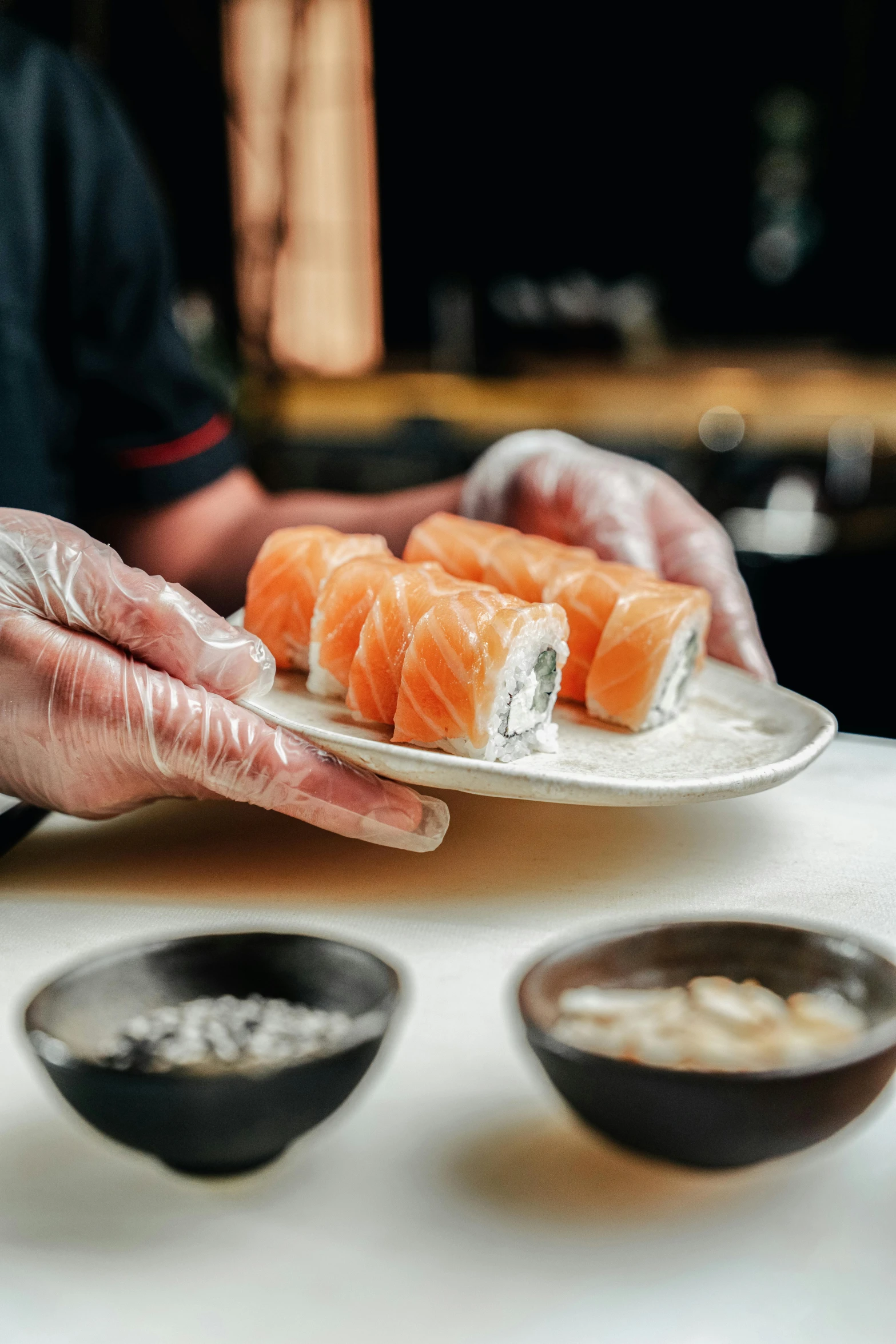 a person holding a plate with sushi on it, back of hand on the table, subtle detailing, foil, four hands