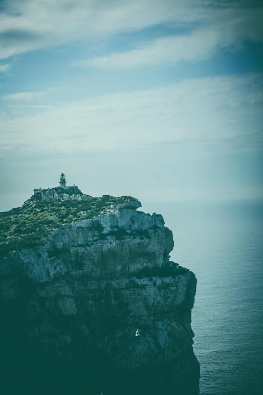 a man standing on top of a cliff next to the ocean, by Daniel Seghers, pexels contest winner, romanticism, lighthouse, costa blanca, slightly minimal, “ aerial view of a mountain