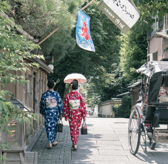 a couple of women walking down a street holding umbrellas, a picture, unsplash, ukiyo-e, red and blue garments, onsen, yukata clothing, sunny day time