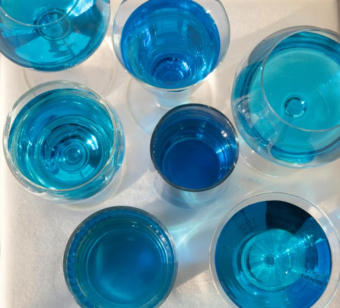 a group of glasses sitting on top of a table, inspired by Évariste Vital Luminais, process art, blue transparent jelly, turquoise, medium blue, high angle close up shot