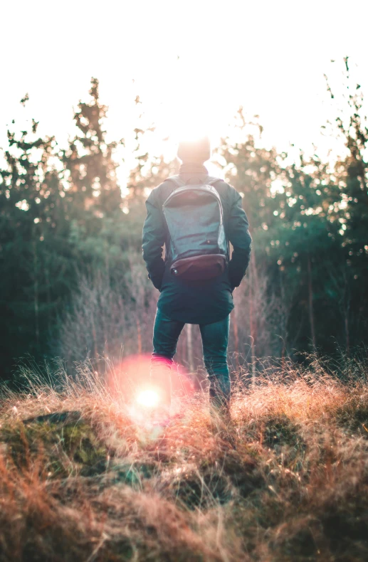 a person standing in a field with a backpack, sunflares;back to camera, looking majestic in forest, overlooking, man standing