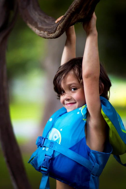 a young boy in a life jacket hanging from a tree branch, a portrait, by Lilia Alvarado, unsplash, avatar image, softplay, sleeveless, with a backpack