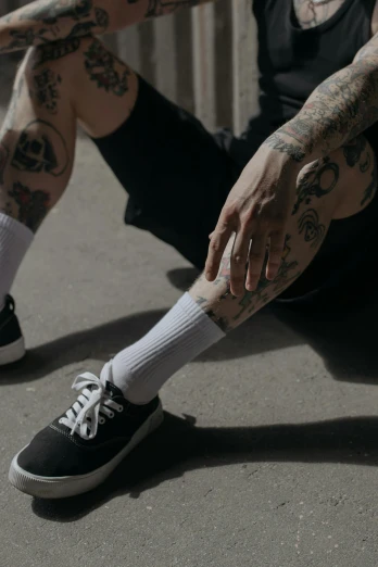 a man with tattoos sitting on the ground, inspired by Seb McKinnon, trending on pexels, wearing white sneakers, swollen veins, blackwork, skateboarding