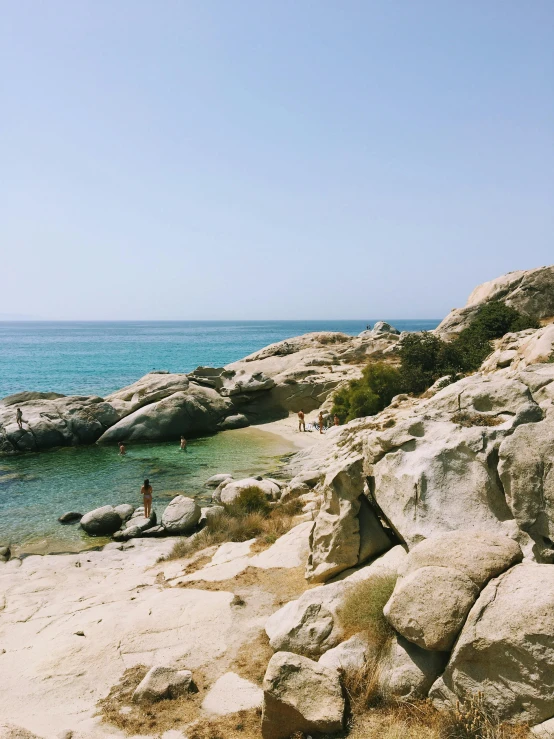 a man standing on top of a beach next to a body of water, by Alexis Grimou, greek pool, boulders, sparsely populated, sparkling cove