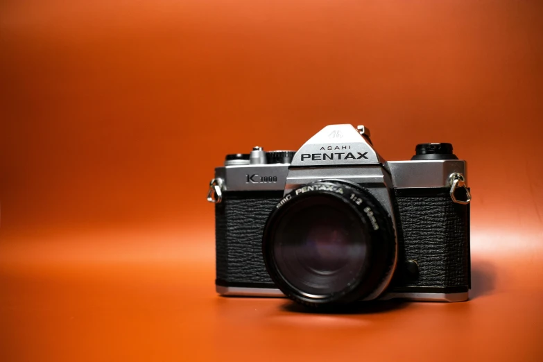 a black and silver camera on an orange background, pexels contest winner, photorealism, pentax, 1980s photography, plain background, profile picture