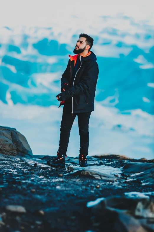 a man standing on top of a snow covered mountain, an album cover, trending on pexels, zayn malik, casual pose, fjords, technologic