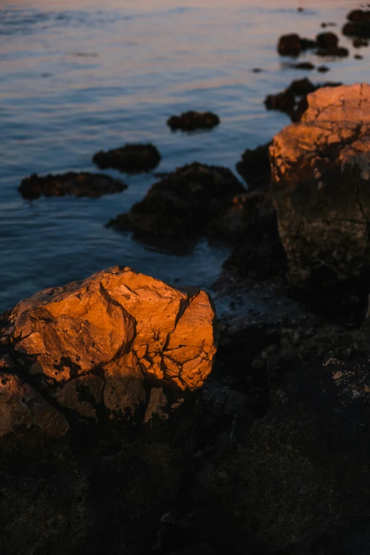 a couple of rocks sitting on top of a body of water, a picture, unsplash, australian tonalism, golden hour 8 k, reddish lava highlights, ((rocks)), late summer evening