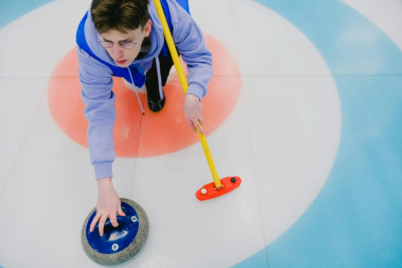 a man holding a curling stick on top of a curling stone, by Julia Pishtar, pexels contest winner, teenage boy, 15081959 21121991 01012000 4k, brilliantly coloured, a high angle shot