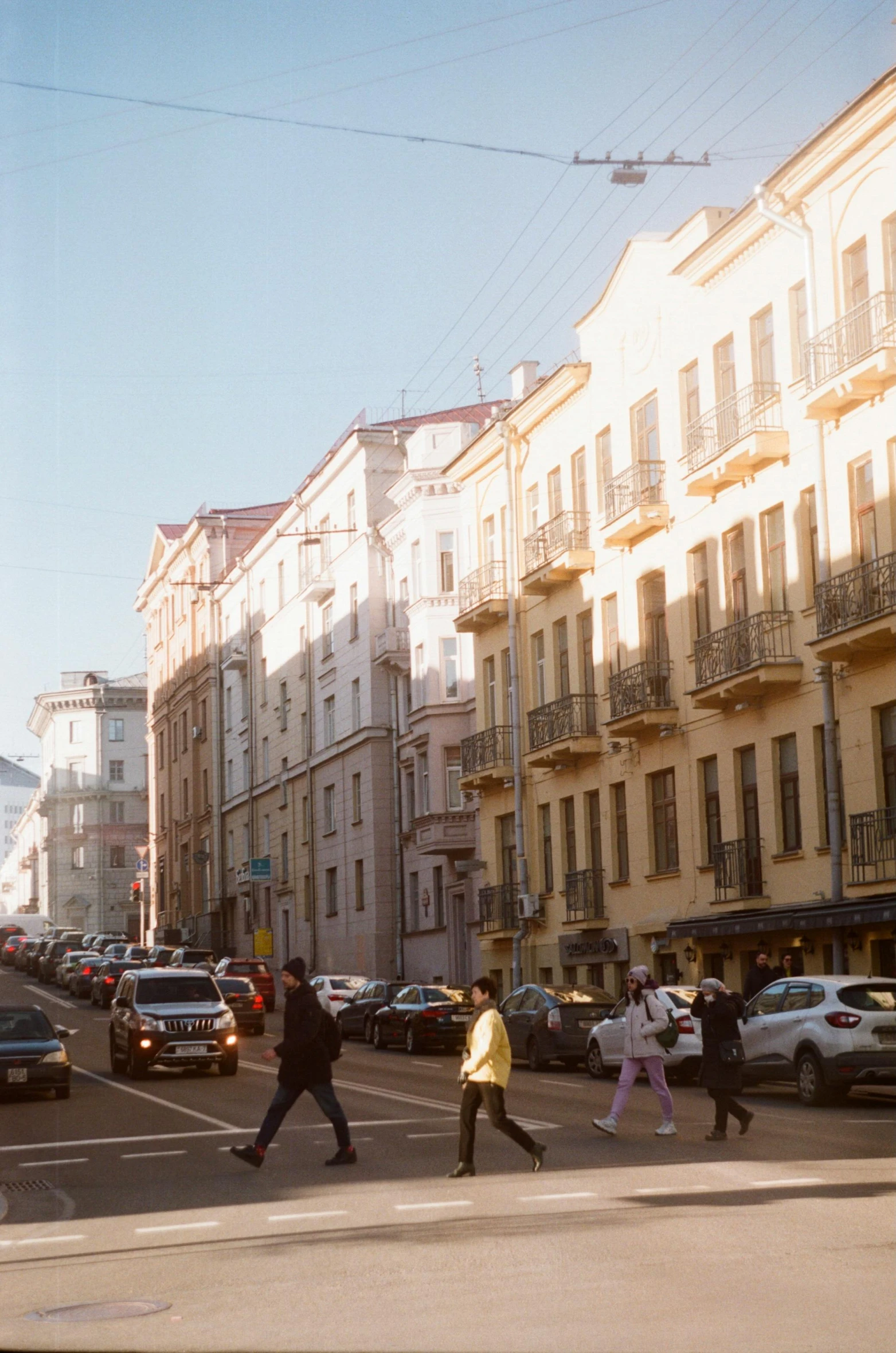 a group of people walking across a street next to tall buildings, inspired by Illarion Pryanishnikov, trending on unsplash, renaissance, saint petersburg, soft golden hour lighting, photo taken on fujifilm superia, white buildings