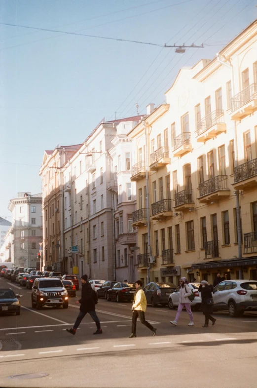 a group of people walking across a street next to tall buildings, inspired by Illarion Pryanishnikov, trending on unsplash, renaissance, saint petersburg, soft golden hour lighting, photo taken on fujifilm superia, white buildings