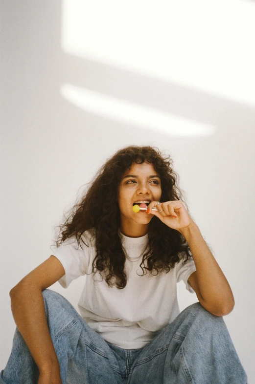 a woman sitting on the floor eating an apple, by Lily Delissa Joseph, trending on pexels, wavy hair yellow theme, young middle eastern woman, sitting on a stool, an all white human
