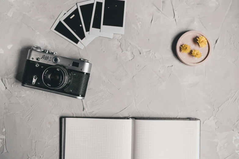 an open book sitting on top of a table next to a camera, charcoal and silver color scheme, notebook, photographic print, rolleiflex